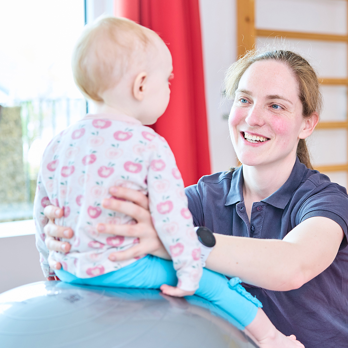 Therapeutin hält sitzendes Baby auf einem Gymnastikball